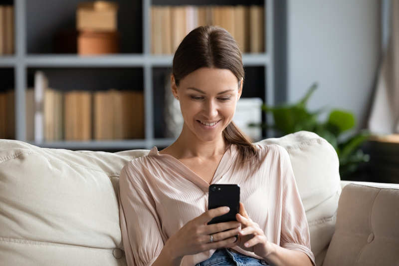 woman sitting on couch in home smiling at phone