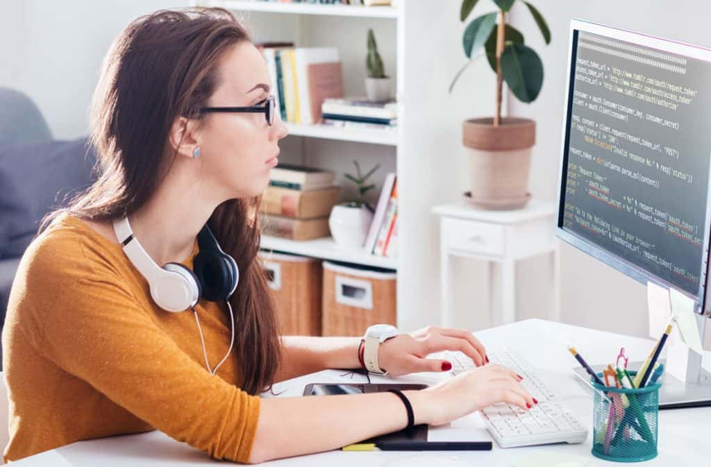 female developer wearing orange sweater coding from a desktop computer in a home office