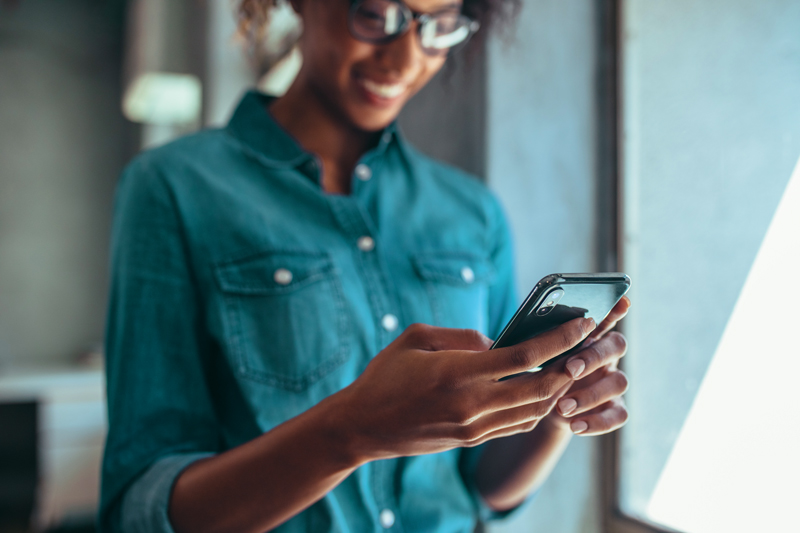 woman on phone standing next to window smiling