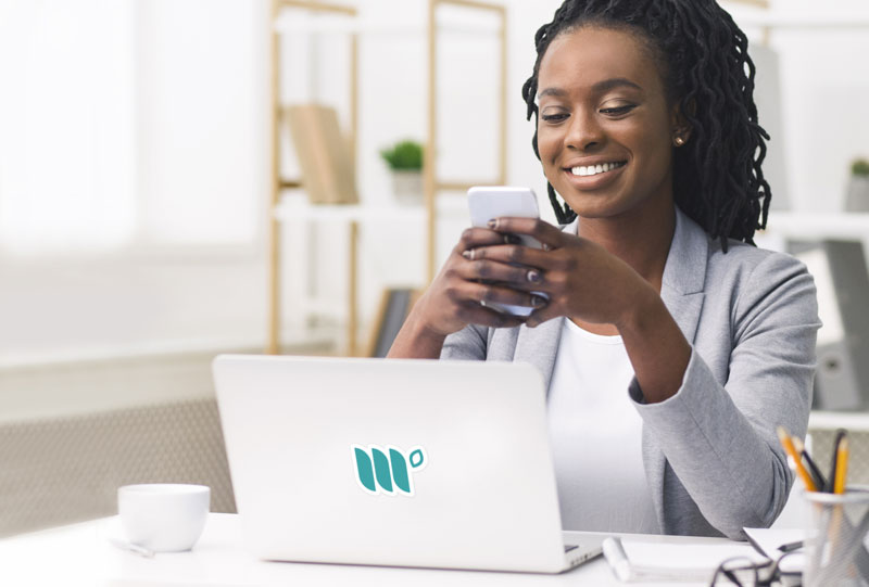woman using phone sitting next to laptop at a desk